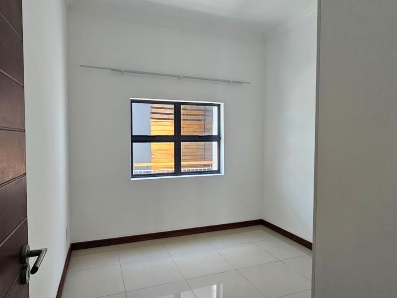A clean, empty bedroom featuring neutral tiled flooring, white walls, and an aluminium-framed window with a fitted curtain rail.