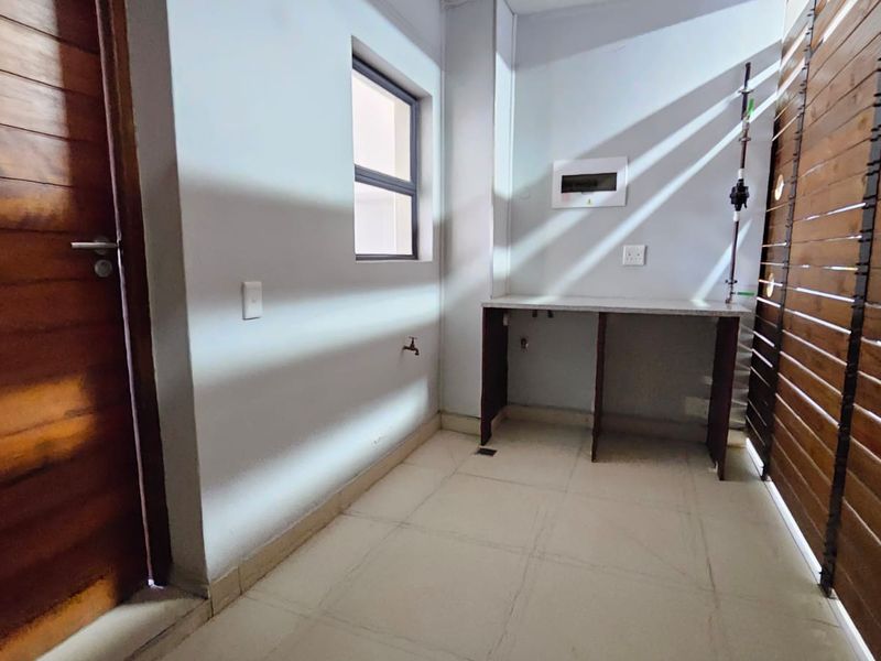 A functional laundry area featuring tiled flooring, a built-in counter with plumbing connections, and a decorative timber slat screen.