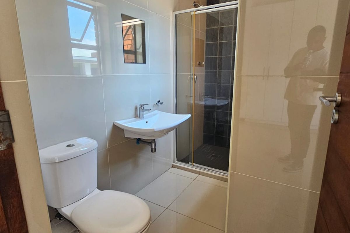 A clean, modern bathroom featuring a wall-mounted basin, toilet, and a glass-enclosed shower with tiled finishes.