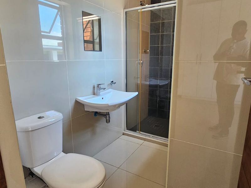 A clean, modern bathroom featuring a wall-mounted basin, toilet, and a glass-enclosed shower with tiled finishes.
