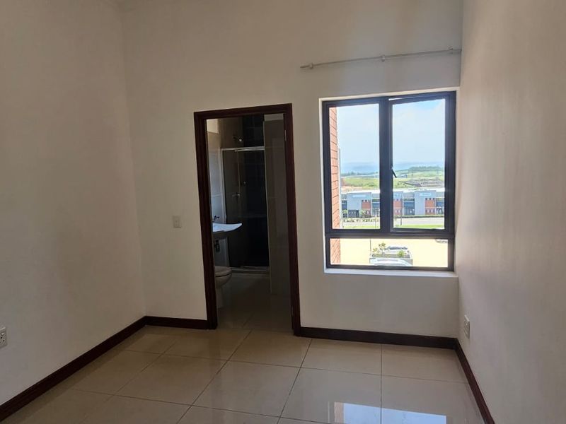 A clean, empty bedroom featuring tiled flooring, a large aluminium window with natural light, and direct access to an en-suite bathroom.