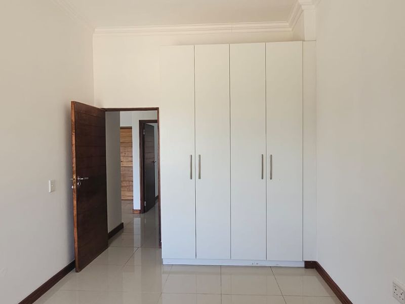 A clean, empty bedroom featuring neutral tiled flooring, white walls, and a modern built-in wardrobe with sleek handles.