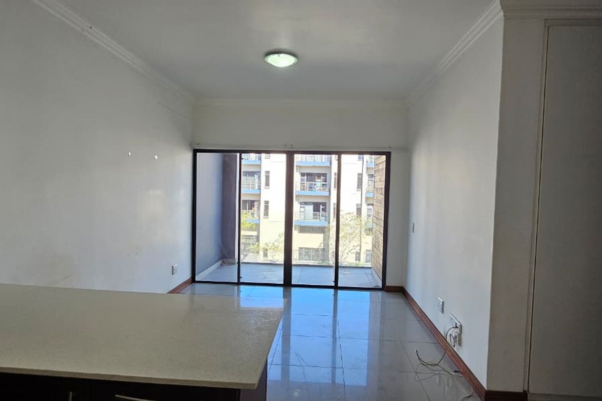 An open-plan living area featuring tiled floors, built-in cupboards, and sliding glass doors leading to a balcony, providing a bright and functional space.