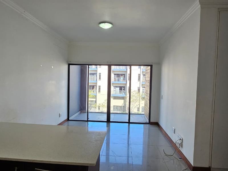 An open-plan living area featuring tiled floors, built-in cupboards, and sliding glass doors leading to a balcony, providing a bright and functional space.