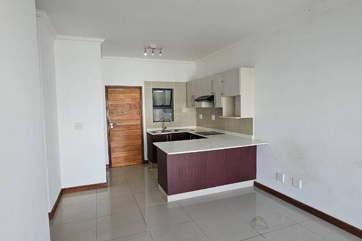 An open-plan kitchen area featuring built-in cabinetry, a hob, and an extractor fan, finished with neutral tiled flooring and clean white walls.