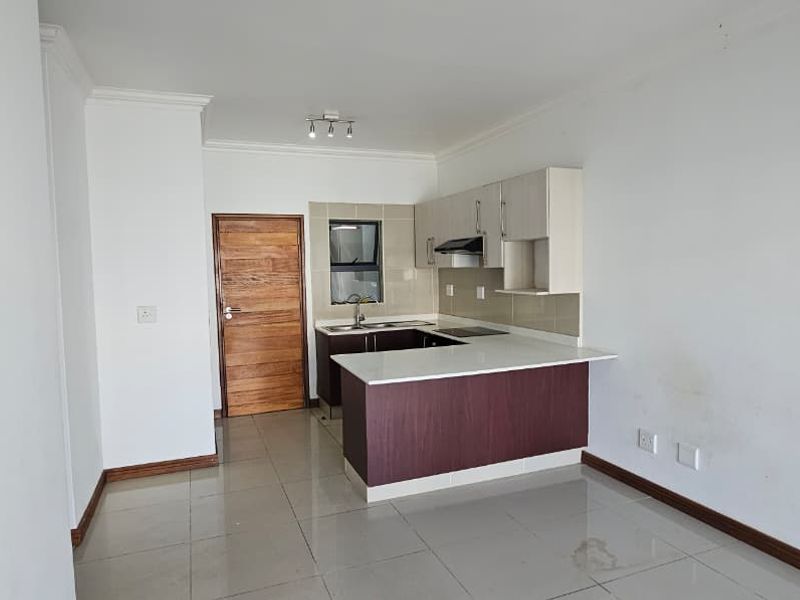 An open-plan kitchen area featuring built-in cabinetry, a hob, and an extractor fan, finished with neutral tiled flooring and clean white walls.