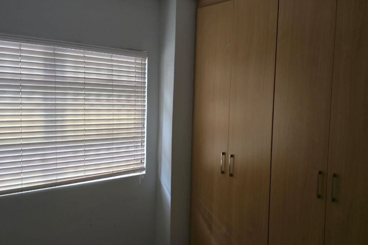 A bedroom featuring built-in wooden wardrobes and venetian blinds, offering a clean and functional space ready for personalization.