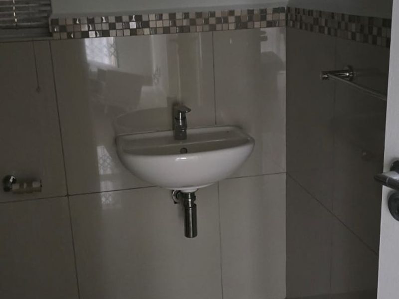 A compact bathroom featuring a wall-mounted basin, chrome fixtures, and tiled finishes, presenting a functional space in need of minor cleaning.