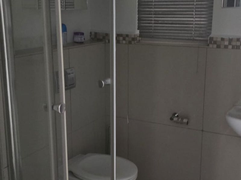 A functional bathroom featuring a glass shower enclosure, wall-mounted toilet, and neutral tiled finishes with venetian blinds for privacy.