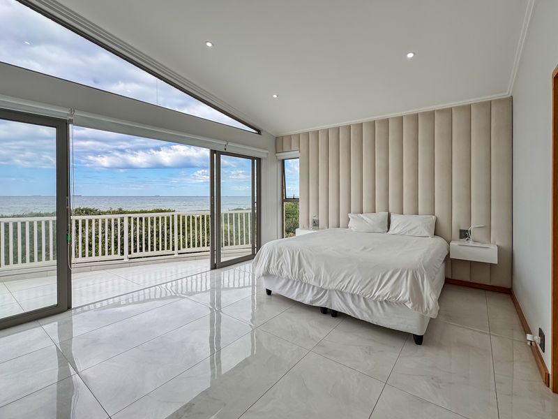 Spacious bedroom featuring large format floor tiles, a custom upholstered headboard wall, and expansive sliding glass doors opening to a balcony with ocean views.