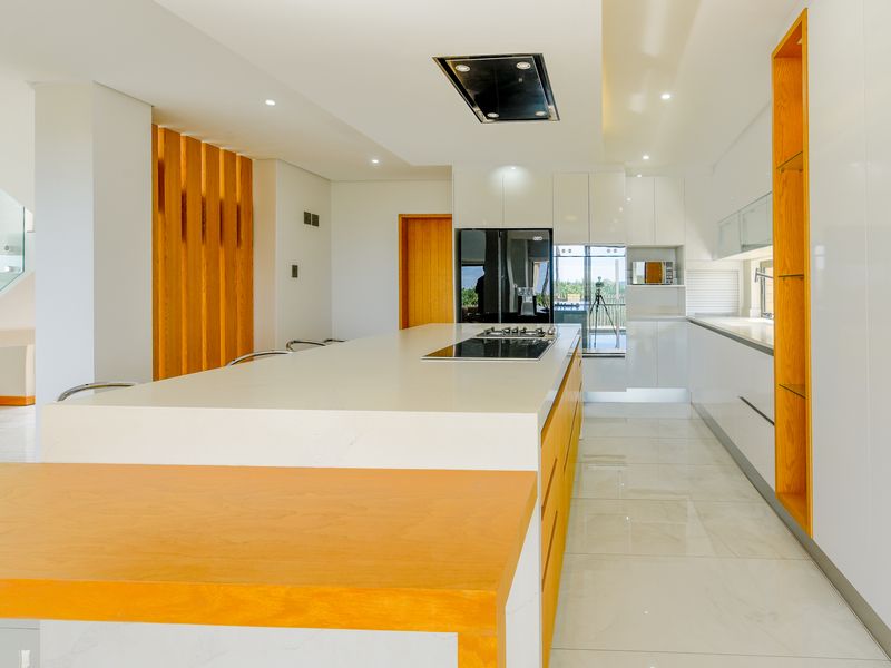 Modern kitchen featuring a large central island with stone countertops, integrated appliances, sleek white cabinetry, and warm wood accents throughout.