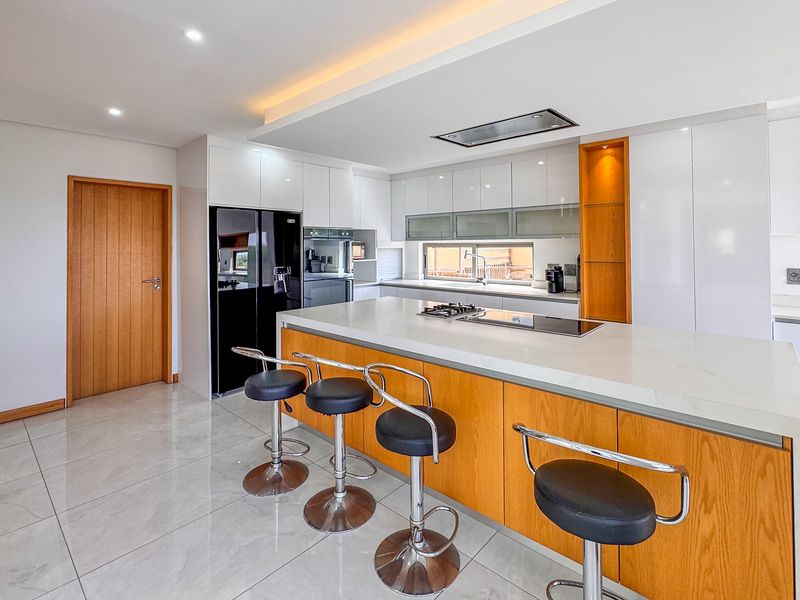 Modern kitchen featuring a large island with stone countertops, built-in gas hob, integrated appliances, and sleek cabinetry with recessed lighting.