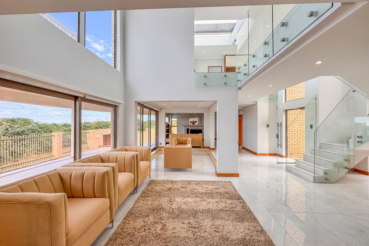 Spacious double-volume living area featuring modern glass balustrades, large sliding doors, polished tile flooring, and abundant natural light from expansive windows and a skylight.
