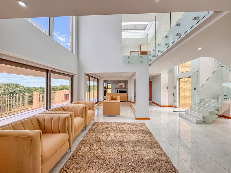 Spacious double-volume living area featuring modern glass balustrades, large sliding doors, polished tile flooring, and abundant natural light from expansive windows and a skylight.