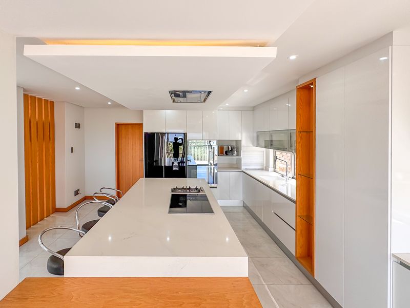 Modern kitchen featuring a large central island with stone countertops, integrated hob, high-gloss cabinetry, and elegant recessed ceiling lighting.