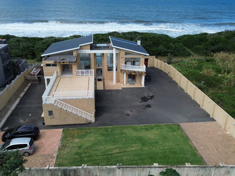 Aerial view of a beachfront property featuring a brick facade, paved driveway, balcony, and direct access to the coastline.