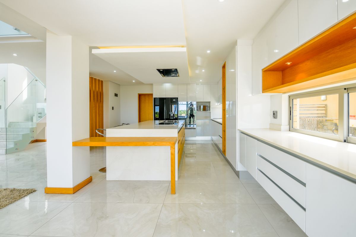 Modern, high-end kitchen featuring a central island, sleek white cabinetry, timber accents, and polished porcelain flooring with integrated lighting.
