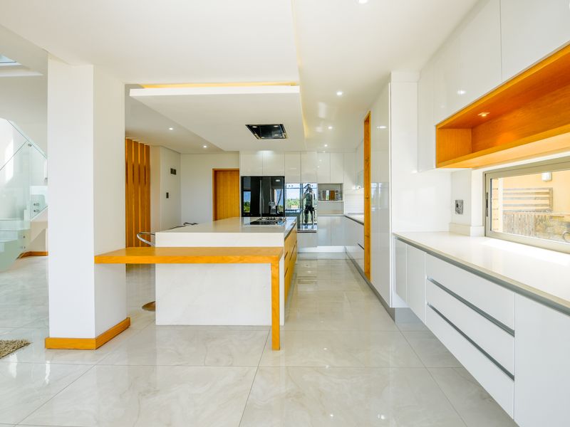 Modern, high-end kitchen featuring a central island, sleek white cabinetry, timber accents, and polished porcelain flooring with integrated lighting.