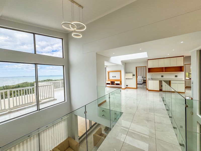 Spacious open-plan living area featuring high ceilings, large windows with ocean views, modern glass balustrades, and a sleek kitchen with built-in cabinetry.