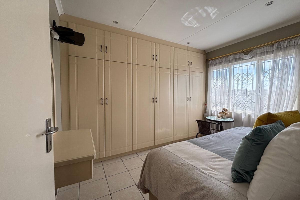 A well-maintained bedroom featuring extensive built-in cupboards, tiled flooring, and a window fitted with security bars for added peace of mind.
