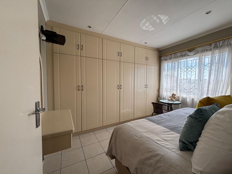A well-maintained bedroom featuring extensive built-in cupboards, tiled flooring, and a window fitted with security bars for added peace of mind.