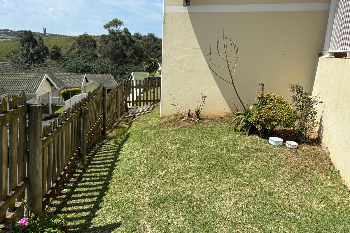 A side garden area featuring a lawn and a wooden picket fence with a view of the surrounding residential estate.