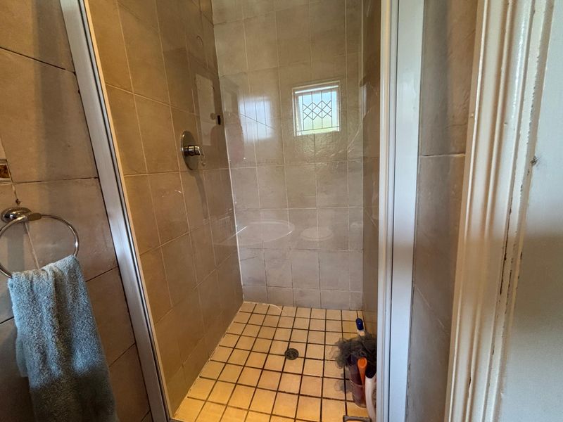 A compact shower stall featuring tiled walls and flooring, equipped with a standard shower mixer and a small window with security bars.