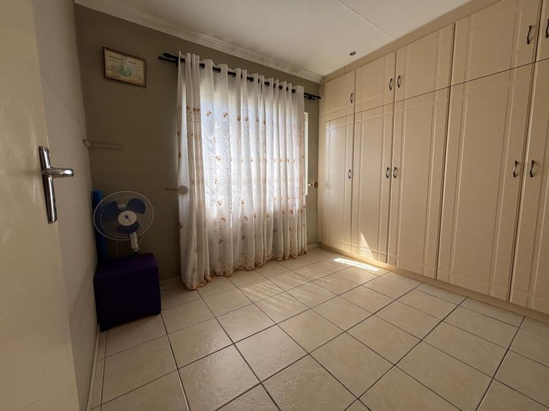 A functional bedroom featuring neutral tiled flooring and extensive built-in cupboard storage, offering a clean and versatile space.