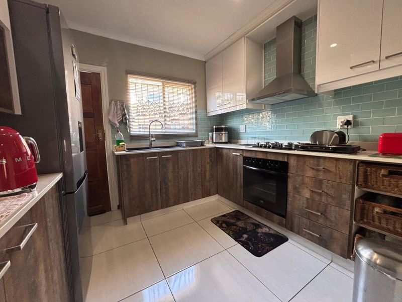 A functional kitchen featuring wood-look cabinetry, a gas hob with extractor fan, subway tile backsplash, and tiled flooring.