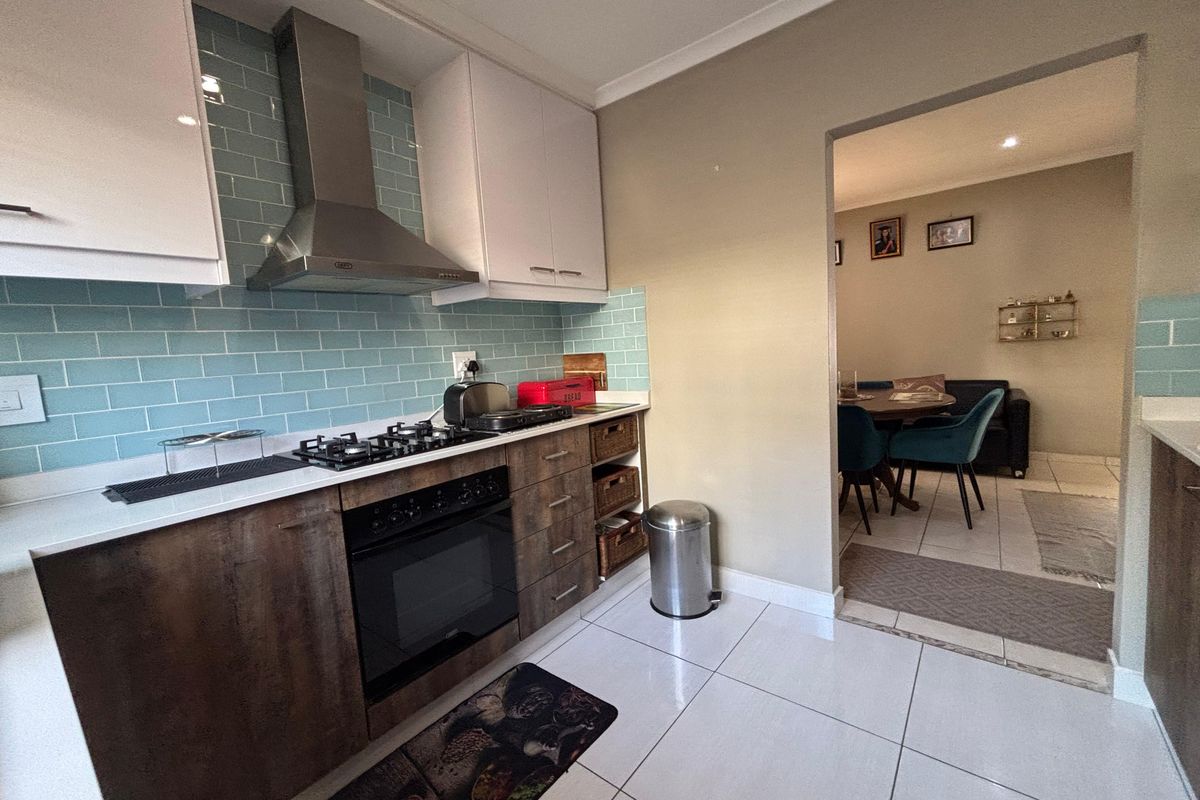 Modern kitchen featuring a gas hob, built-in oven, stainless steel extractor fan, subway tile backsplash, and stone countertops, with an open flow to the dining area.
