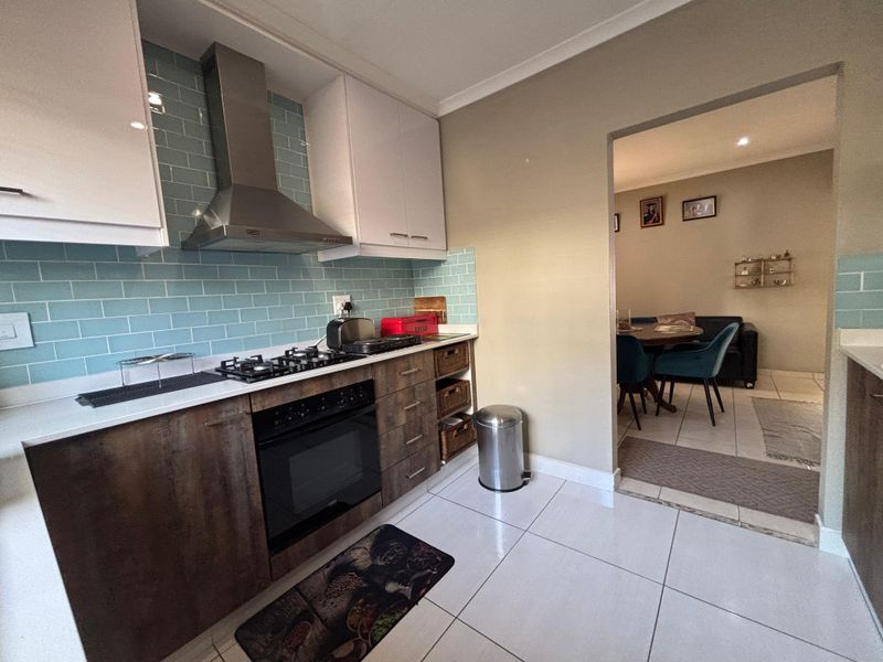 Modern kitchen featuring a gas hob, built-in oven, stainless steel extractor fan, subway tile backsplash, and stone countertops, with an open flow to the dining area.