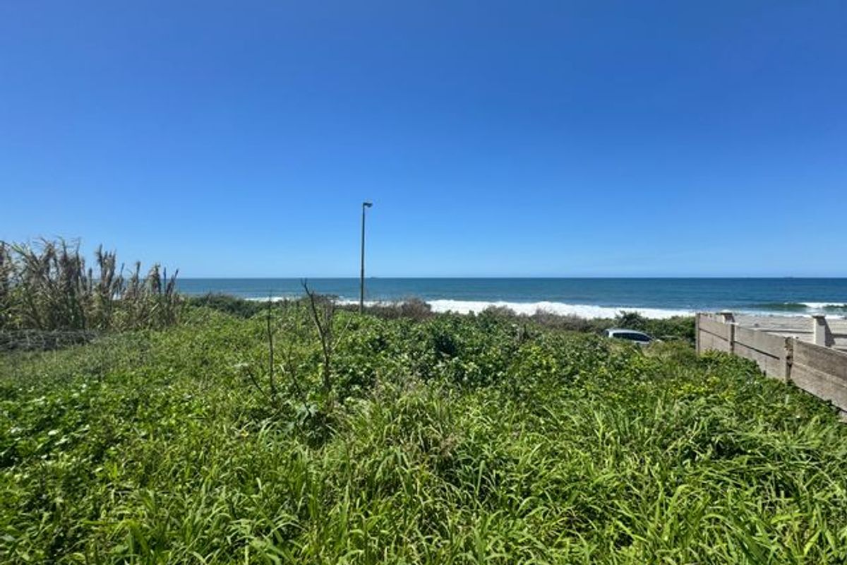 A view of the ocean from a vacant residential plot featuring natural vegetation and a concrete boundary wall.