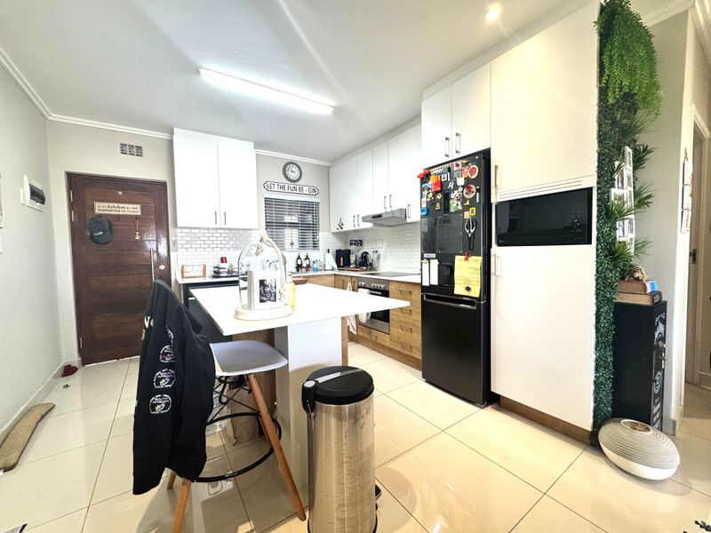 Modern kitchen featuring white and wood-tone cabinetry, subway tile backsplash, built-in oven, hob, extractor fan, and a central kitchen island with tiled flooring.