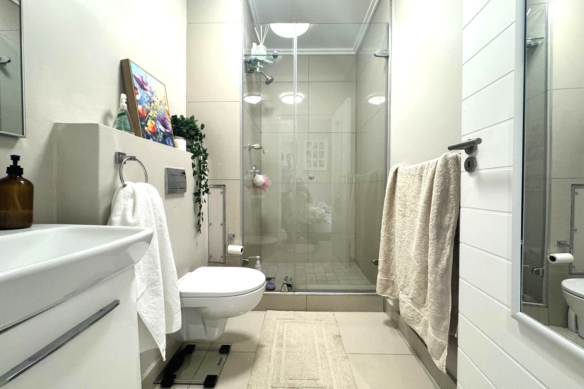 Modern bathroom featuring a wall-hung toilet with concealed cistern, a glass-enclosed shower, and contemporary tiled finishes.