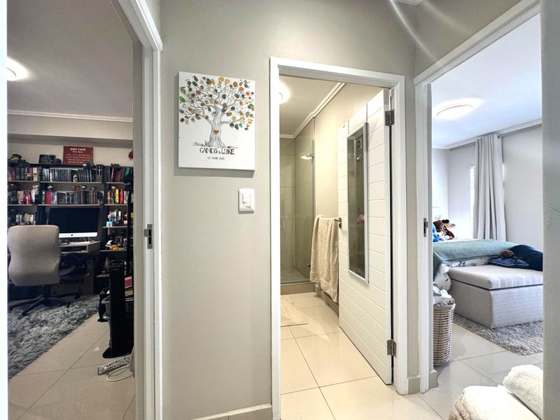 A well-maintained hallway providing access to a home office, a bathroom with a glass shower, and a bedroom.