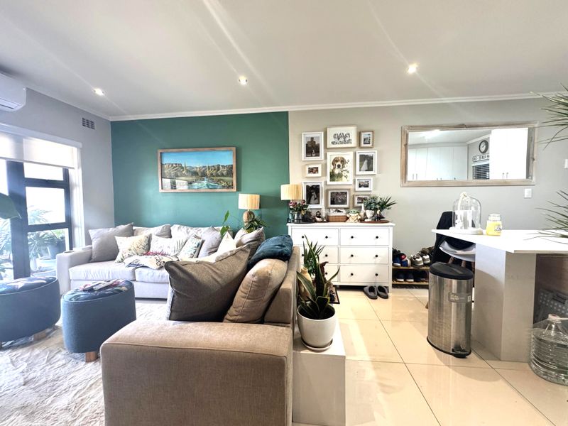 An open-plan living area featuring tiled flooring, recessed downlights, an air conditioning unit, and a kitchen island, creating a bright and functional space.