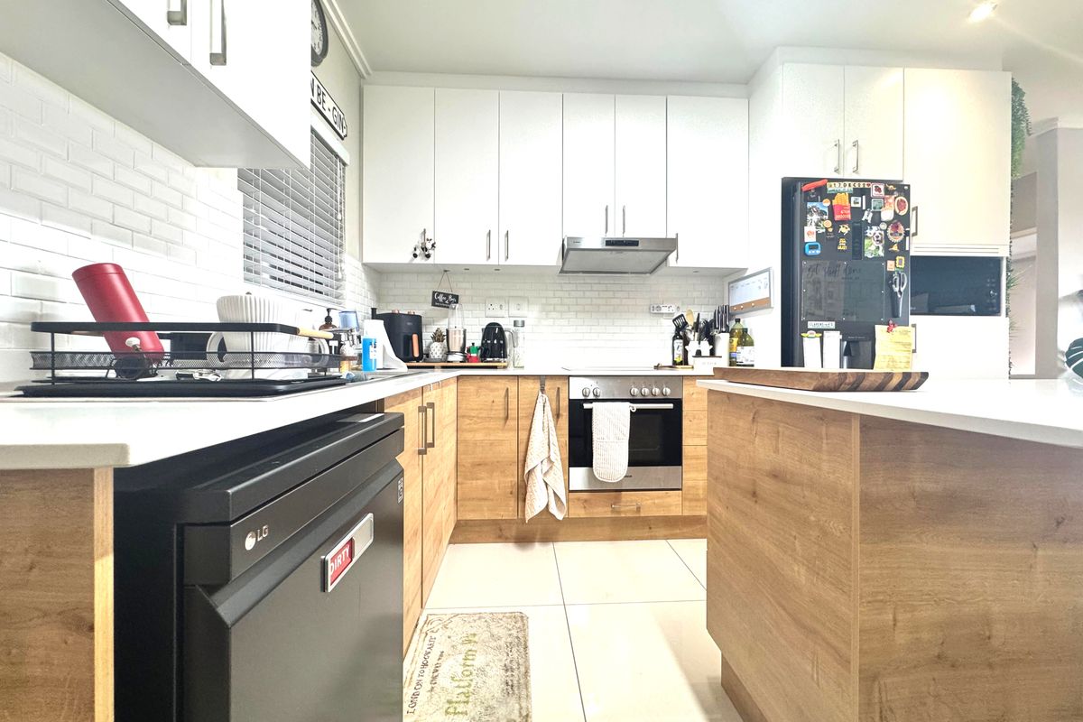Modern kitchen featuring light wood-tone lower cabinetry, white upper cabinets, subway tile backsplash, stone countertops, and a functional kitchen island.