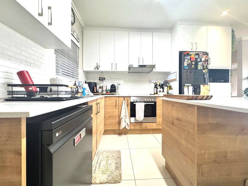 Modern kitchen featuring light wood-tone lower cabinetry, white upper cabinets, subway tile backsplash, stone countertops, and a functional kitchen island.