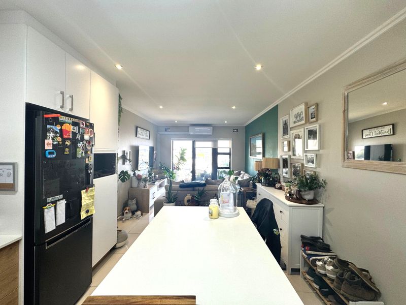 An open-plan living and kitchen area featuring modern white cabinetry, tiled flooring, recessed lighting, and a split-system air conditioner leading to a balcony.