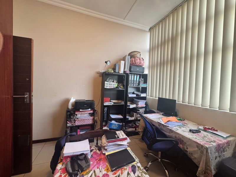 A functional office space featuring tiled flooring and vertical window blinds, providing a practical area for work or study.