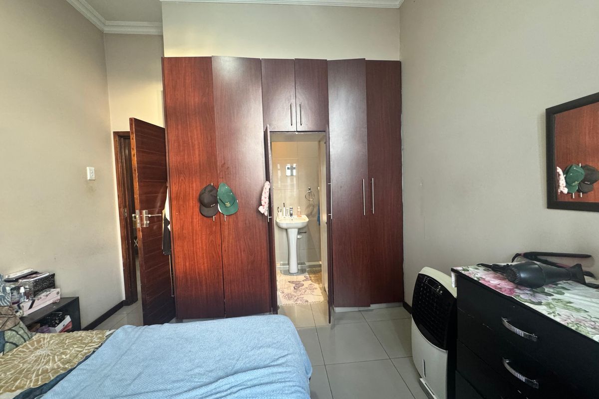Bedroom featuring built-in wooden cupboards and an en-suite area with a pedestal basin, finished with neutral wall paint and tiled flooring.