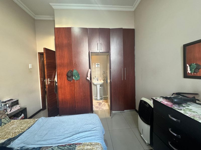 Bedroom featuring built-in wooden cupboards and an en-suite area with a pedestal basin, finished with neutral wall paint and tiled flooring.