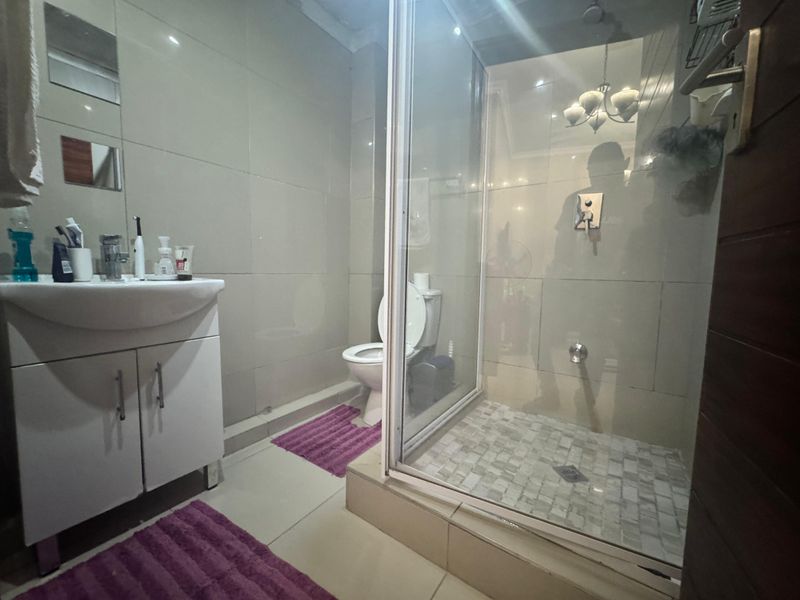 A functional bathroom featuring a vanity cabinet with basin, a toilet, and a glass-enclosed shower with tiled finishes.