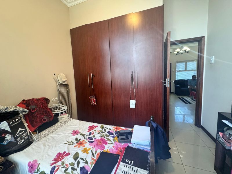 A bedroom featuring built-in wooden cupboards and tiled flooring, with a doorway leading to an adjacent living area.