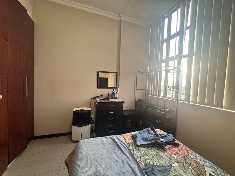 A bedroom featuring tiled flooring, a built-in wardrobe, and a large window with vertical blinds allowing natural light.