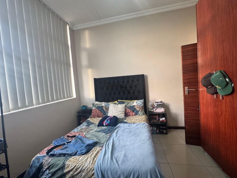 A bedroom featuring tiled flooring, a built-in wooden wardrobe, and vertical window blinds.