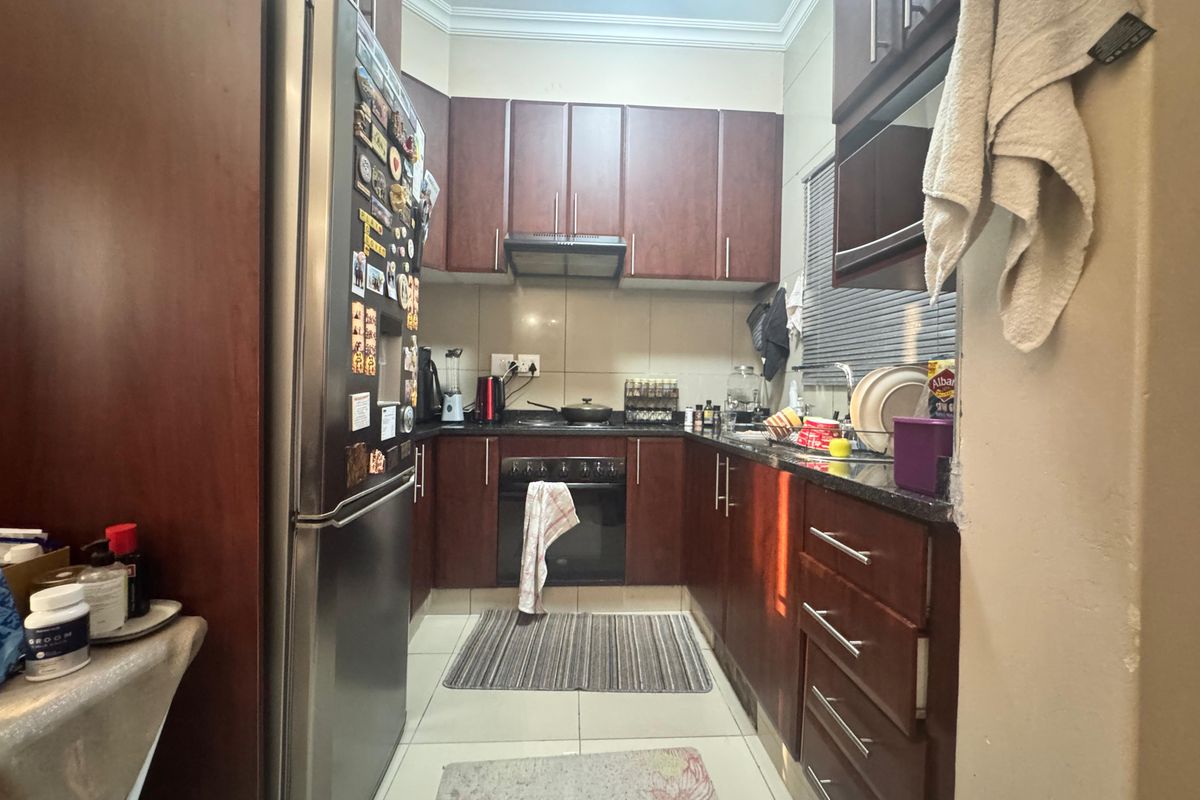 A compact kitchen featuring dark wood cabinetry, granite countertops, and built-in appliances, offering a functional layout with tiled flooring.