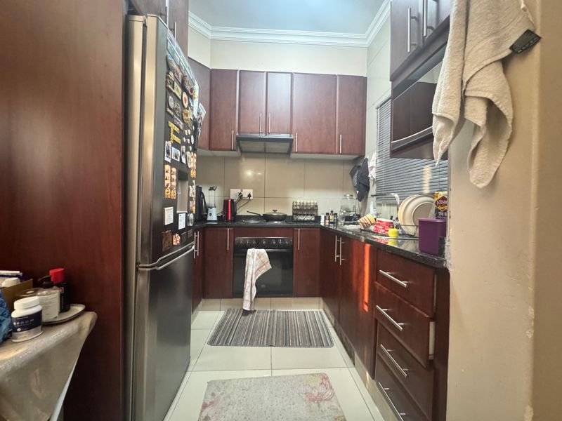 A compact kitchen featuring dark wood cabinetry, granite countertops, and built-in appliances, offering a functional layout with tiled flooring.