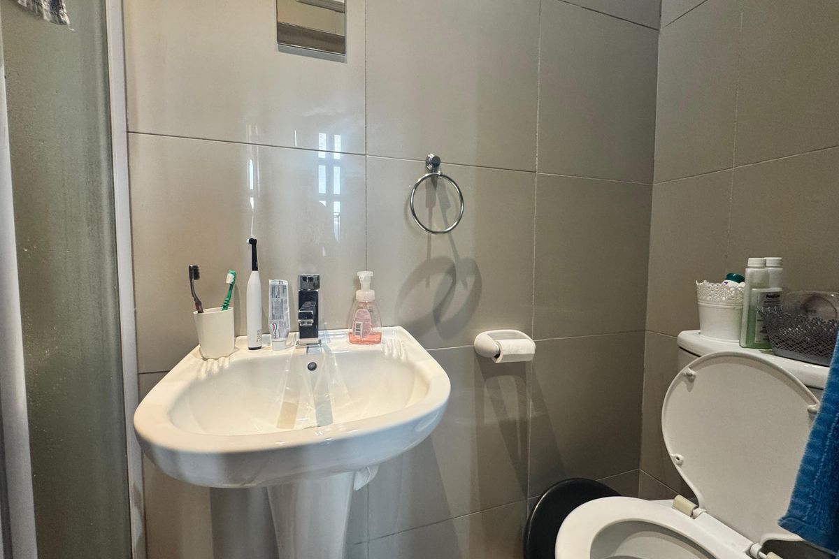 A functional bathroom featuring a pedestal sink, toilet, and full-height wall tiling with a shower enclosure.