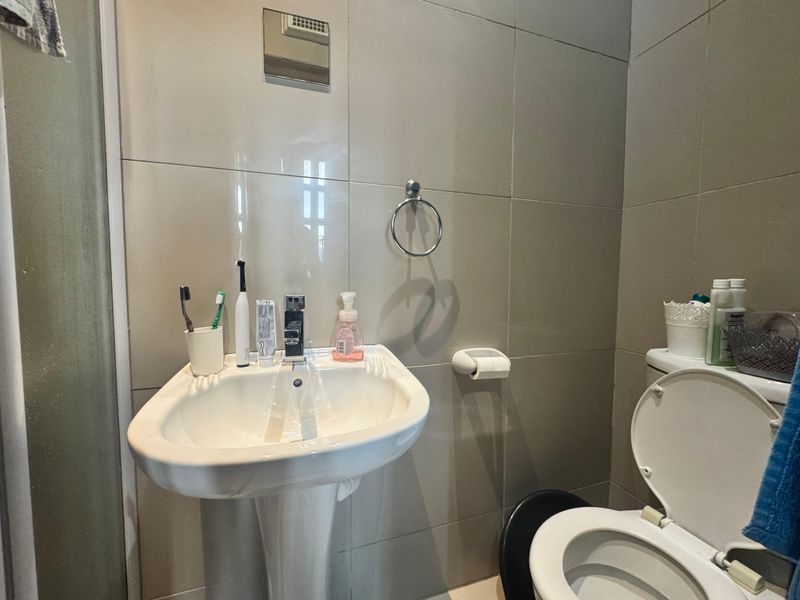 A functional bathroom featuring a pedestal sink, toilet, and full-height wall tiling with a shower enclosure.